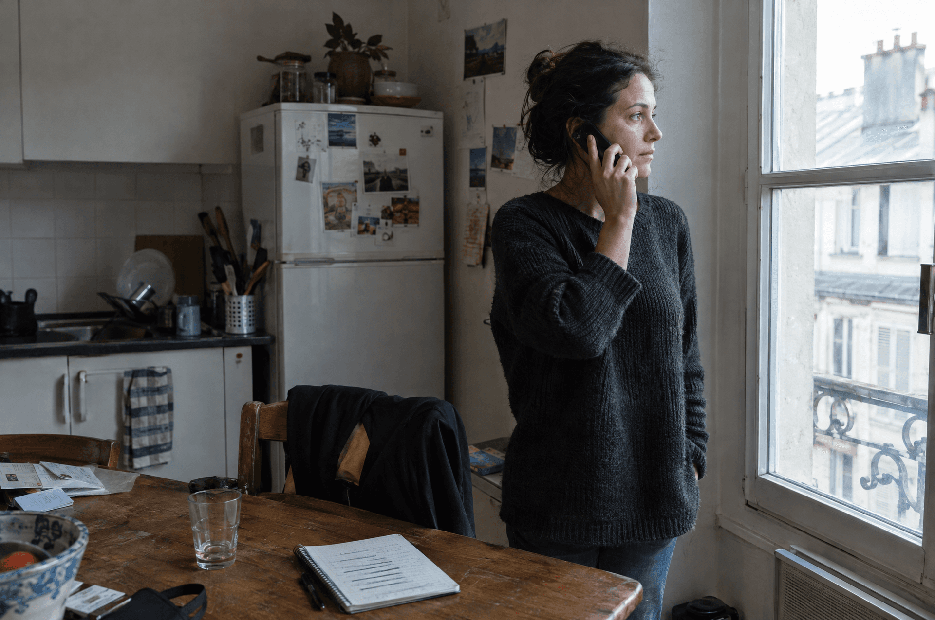 Une femme au téléphone dans sa cuisine, un carnet ouvert devant elle.