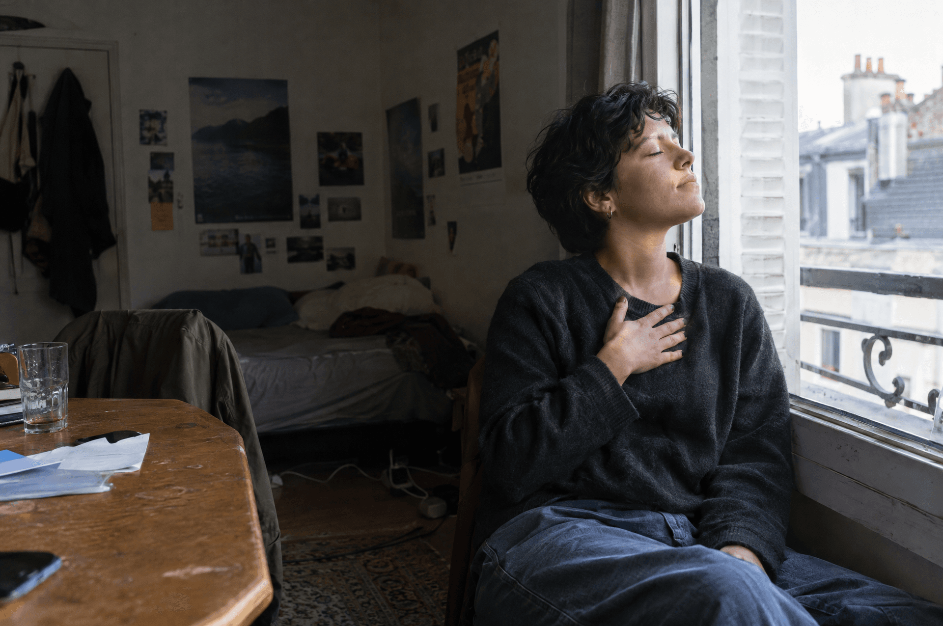 Une personne assise près d'une fenêtre ouverte, les yeux fermés, une main sur la poitrine.
