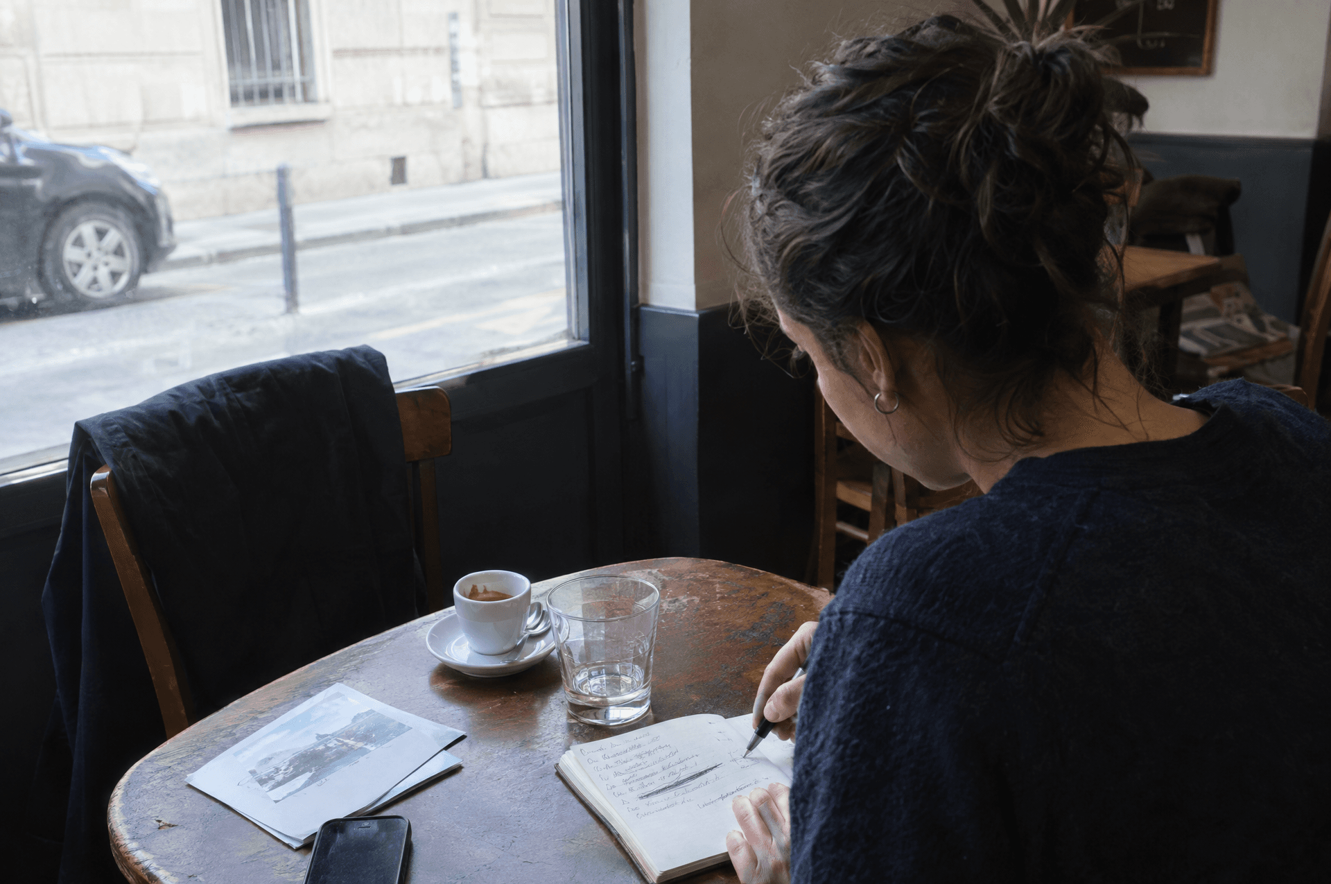 Une femme qui écrit et rature dans un carnet à une table de café.