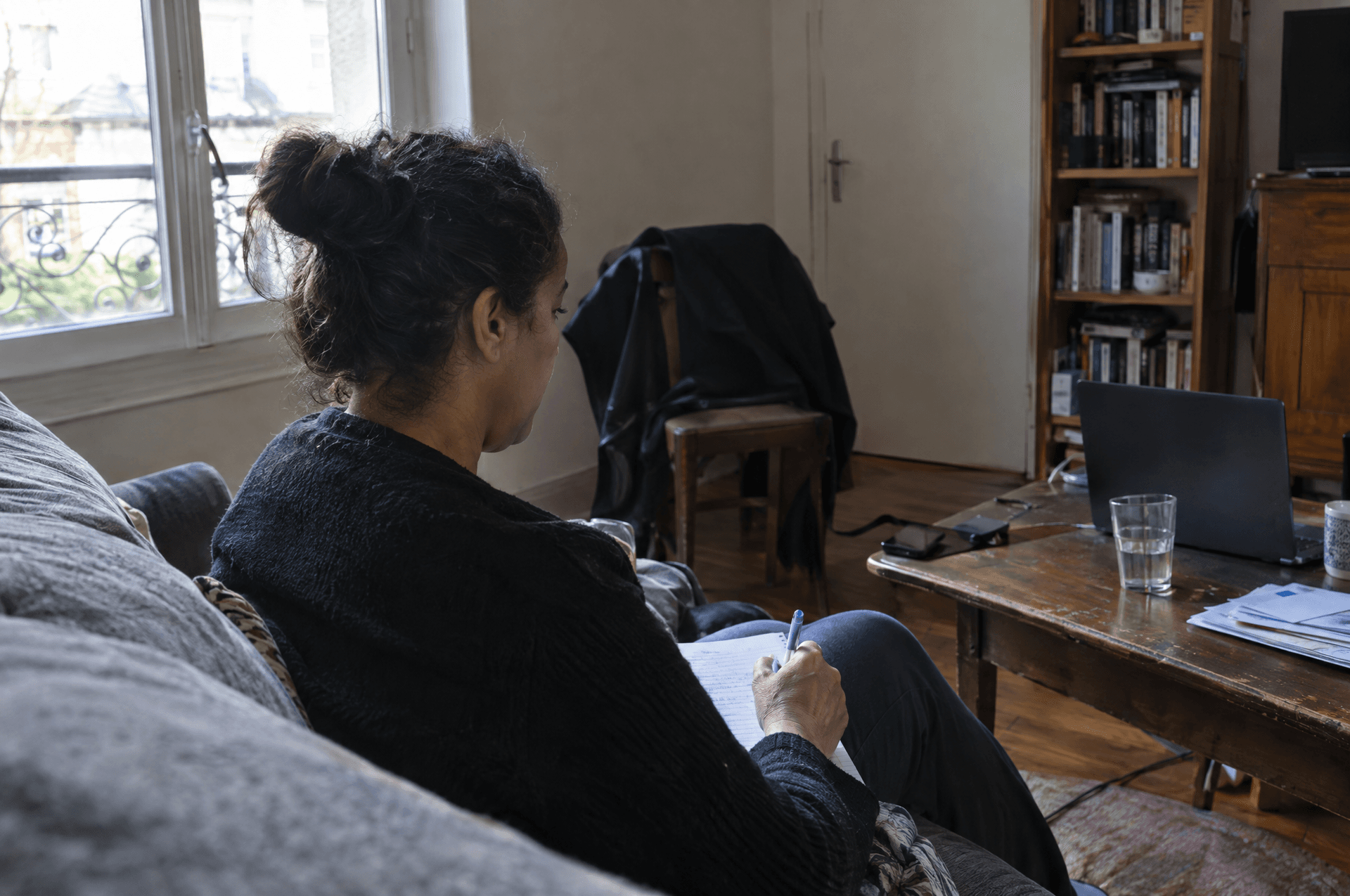 Une femme sur son canapé qui prend des notes pendant une séance en ligne.